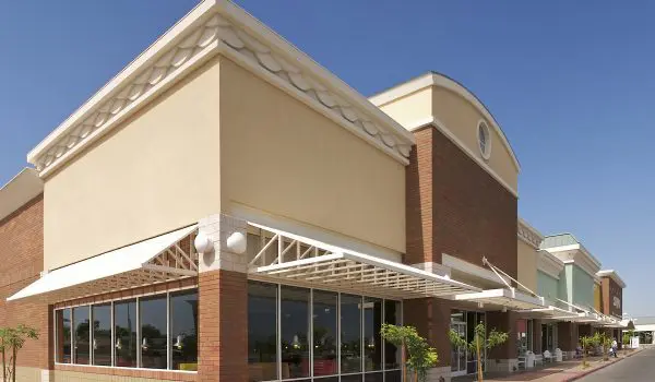 A modern retail building with a covered walkway, large windows, and an arched entrance under a clear blue sky.