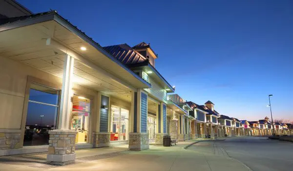 A row of illuminated storefronts under a dusk sky.