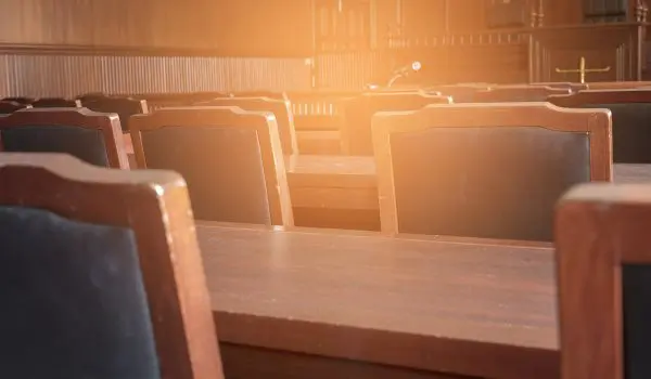Empty wooden chairs and desks are basking in the warm glow of sunlight, suggesting a peaceful setting, perhaps in a lecture hall or courtroom.