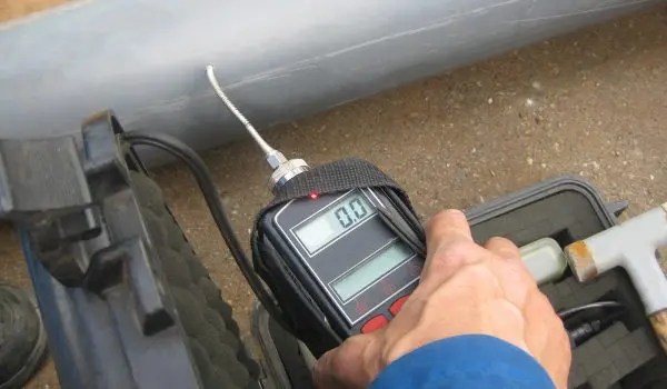 A person's hand is holding a digital tire tread depth gauge against a tire to measure its tread depth.