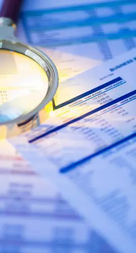 A magnifying glass and calculator are placed on top of a collection of financial documents and charts.