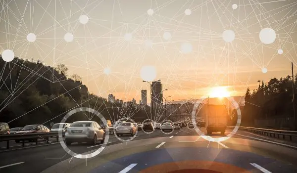 A highway at sunset is overlaid with digital network symbols representing connectivity or communication.
