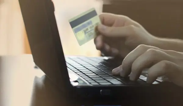 A person is typing on a laptop while holding a credit card.