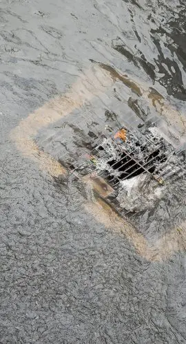 Water flows around a storm drain on a wet street.