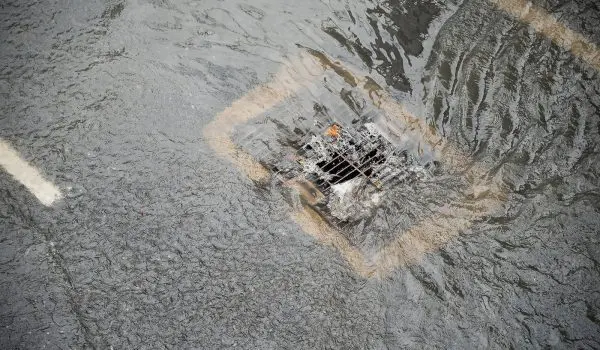 Water flows around a storm drain on a wet street.