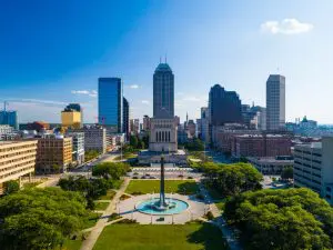 Aerial view of a city skyline with a park and a prominent fountain in the foreground under a clear blue sky.