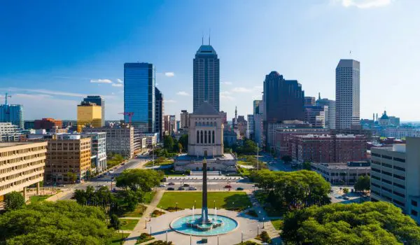 Aerial view of a city skyline with a park and a prominent fountain in the foreground under a clear blue sky.