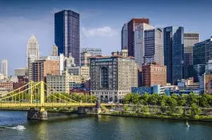 A vibrant cityscape with skyscrapers, a bridge across a river, and clear blue skies.