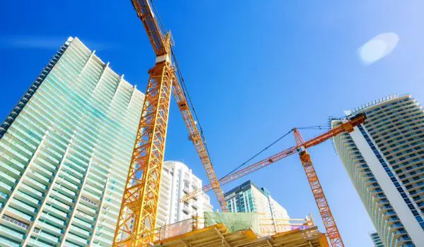 A construction site with scaffolding, cranes, and tall buildings under a blue sky.