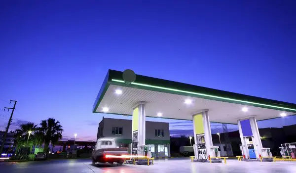A gas station is illuminated at dusk with a clear blue sky in the background.