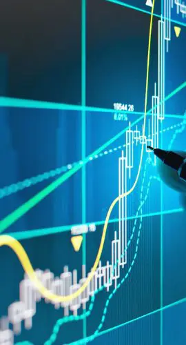 A hand holding a pen points to a luminous stock market graph on a digital screen, suggesting a focus on financial analysis or trading activities.