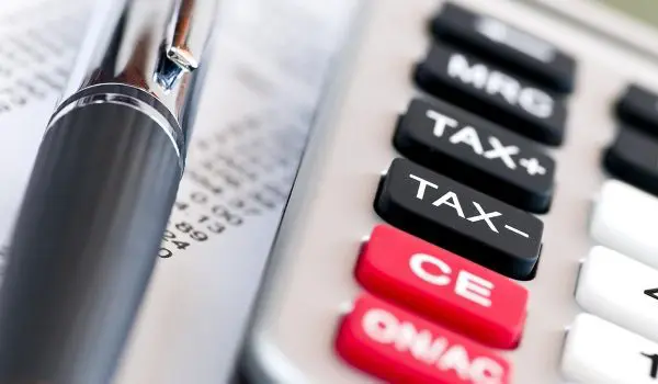 A calculator with a prominent red "TAX" button is lying next to a pen on top of financial documents.