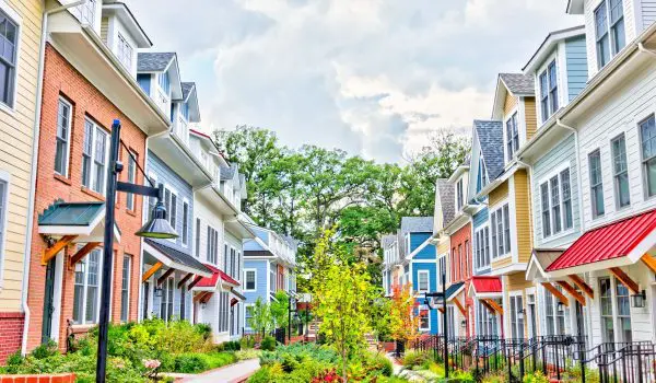A row of colorful suburban townhouses with front porches and a landscaped pathway under a partly cloudy sky.