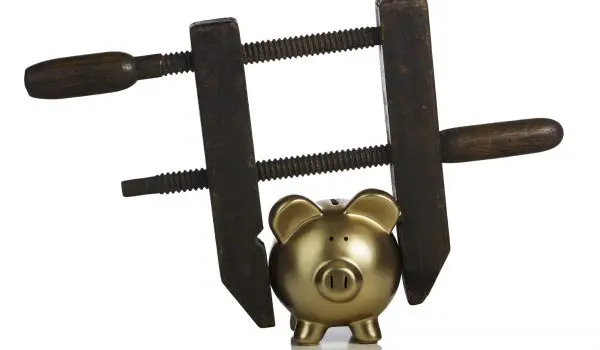 A gold piggy bank is being squeezed by a carpenter's vise with wooden handles.