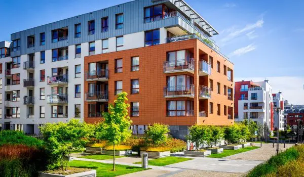 Modern apartment buildings with vibrant facades are surrounded by neatly landscaped green spaces and pedestrian paths under a clear blue sky.
