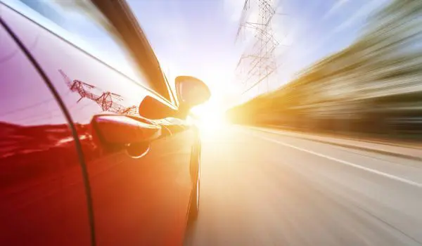 A red car is speeding down a road, with a blurred background indicating high speed and motion.