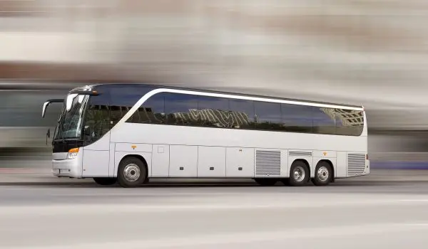 A white coach bus is in motion with a blurred background conveying the sense of speed.
