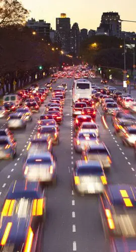 A bustling city street at dusk with blurred vehicles indicating heavy traffic and motion.