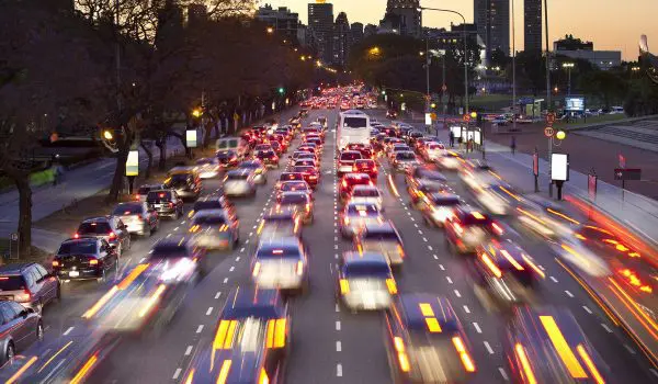 A bustling city street at dusk with blurred vehicles indicating heavy traffic and motion.