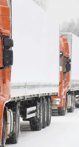 A red semi-truck is driving on a snow-covered road.
