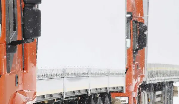 A red semi-truck is driving on a snow-covered road.