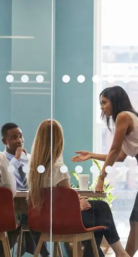 A group of colleagues is having a meeting in a modern office space with large windows.