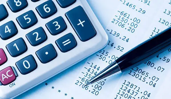 A calculator and a pen lie atop financial documents with numerical data.