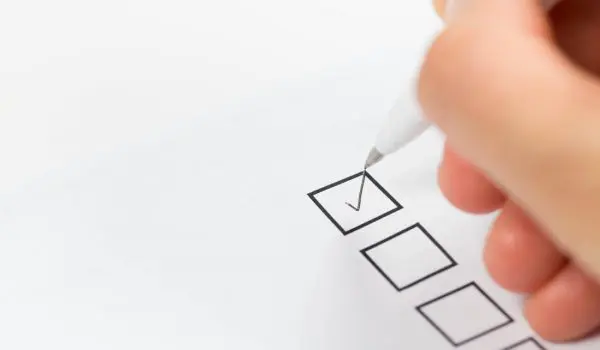 A hand holding a pen appears to be ticking a checkbox on a paper form.