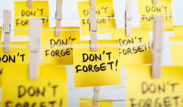 Multiple yellow sticky notes with "DON'T FORGET!" written on them are attached to a string by wooden clothespins.