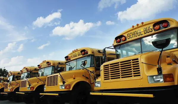 A row of yellow school buses is parked under a blue sky with scattered clouds.