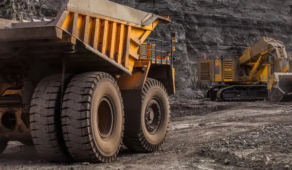 Large mining trucks and machinery operate in a rocky excavation site.