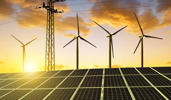 Solar panels and wind turbines are positioned against a backdrop of a dramatic sunset sky, illustrating a clean energy concept.