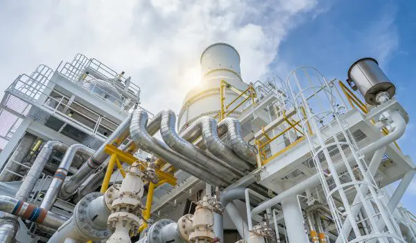 An industrial facility with a complex arrangement of pipes, steel structures, and equipment under a blue sky with clouds.
