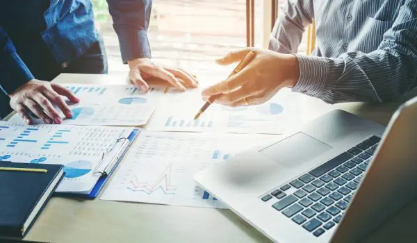 Professionals are engaged in a discussion over documents with charts and data, with a laptop and other office materials on the table.