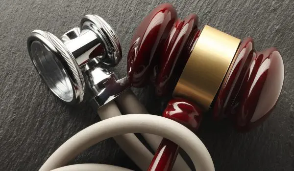 A close-up of three stethoscopes with silver chest pieces and tubes in shades of white and red, resting on a textured dark surface.