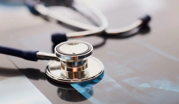 A stethoscope lies atop a reflective surface with an X-ray film beneath it.