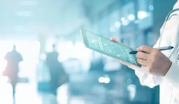 A healthcare professional is examining a digital tablet x-ray with a blurred hospital corridor in the background.