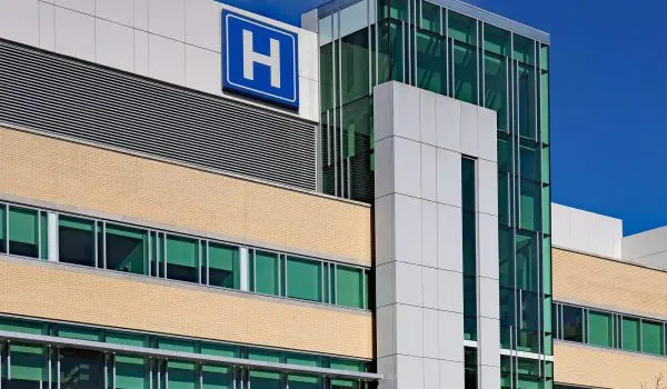 A modern hospital building with a large blue "H" sign indicating it is a medical facility.