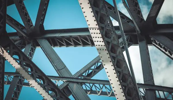 A close-up view of a steel bridge structure against a blue sky with clouds.