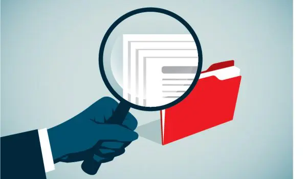 A magnifying glass is being held over a folder with papers, emphasizing scrutiny or examination.