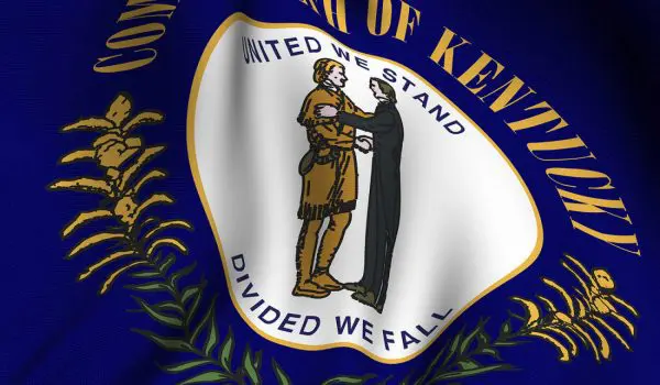 A close-up of the flag of Kentucky featuring a seal with two figures shaking hands surrounded by the state's motto and a wreath of goldenrod.