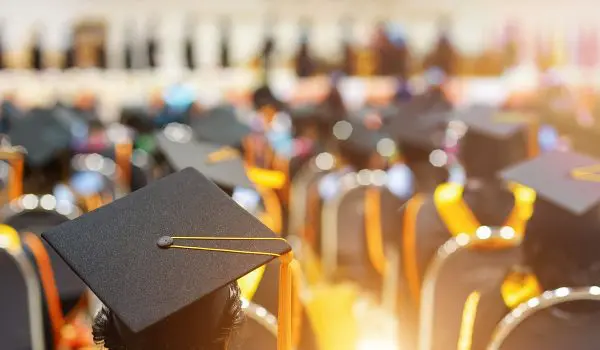 Graduation caps atop heads in a ceremony with sunlit chairs indicating a commencement event.