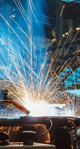 A welder is working on a metal piece, creating bright sparks as they work.