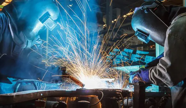 A welder is working on a metal piece, creating bright sparks as they work.