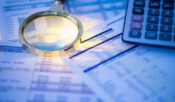 A magnifying glass lies on top of financial documents next to a calculator, suggesting a detailed financial analysis or audit.