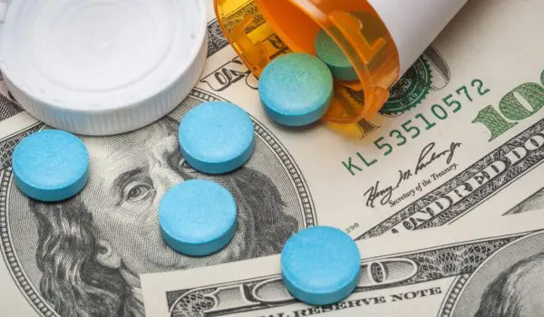 Prescription pills are scattered on a background of US dollar bills next to an open pill bottle and a prescription receipt.