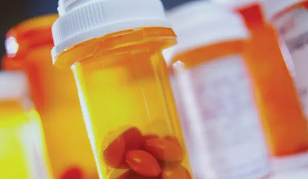 Several prescription medication bottles with orange safety caps, some containing pills, are in focus against a blurred background.