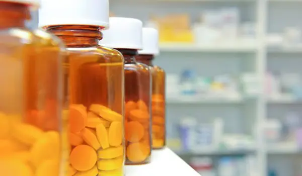 Orange prescription bottles filled with pills are lined up on a pharmacy shelf, with a focus on the closest bottle and a blurred background.