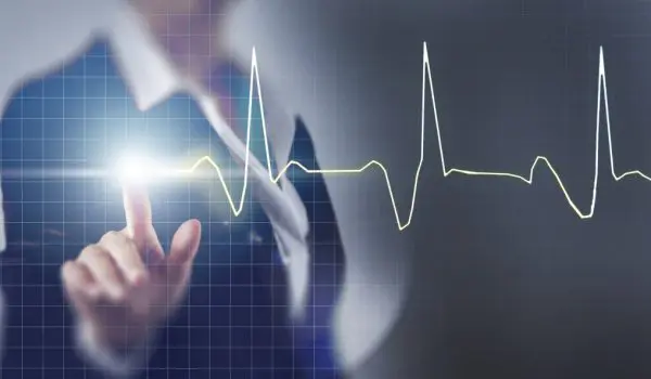 A person in a business suit is pointing at a holographic projection of a heartbeat pulse line chart.