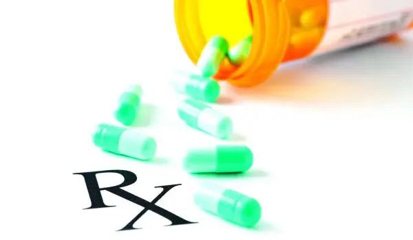 A spilled bottle of green capsules next to a prescription label with the symbol "Rx" visible.